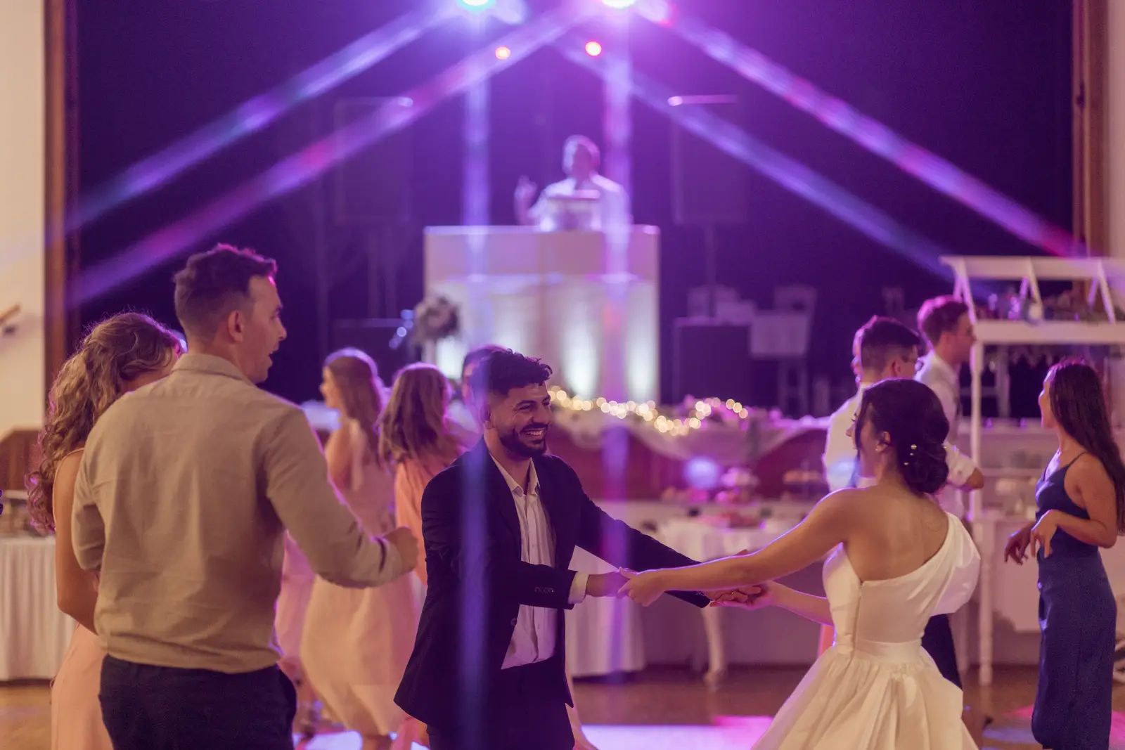 DJ pult lila fénypászmák alatt, előtte táncoló pár